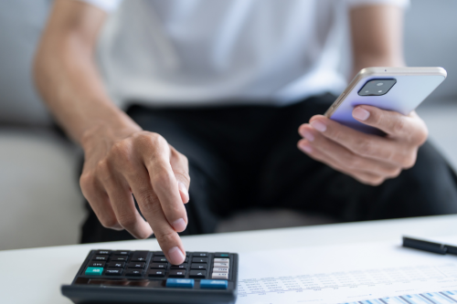 Pessoa a usar calculadora e telemóvel para analisar valores da prestação do crédito habitação